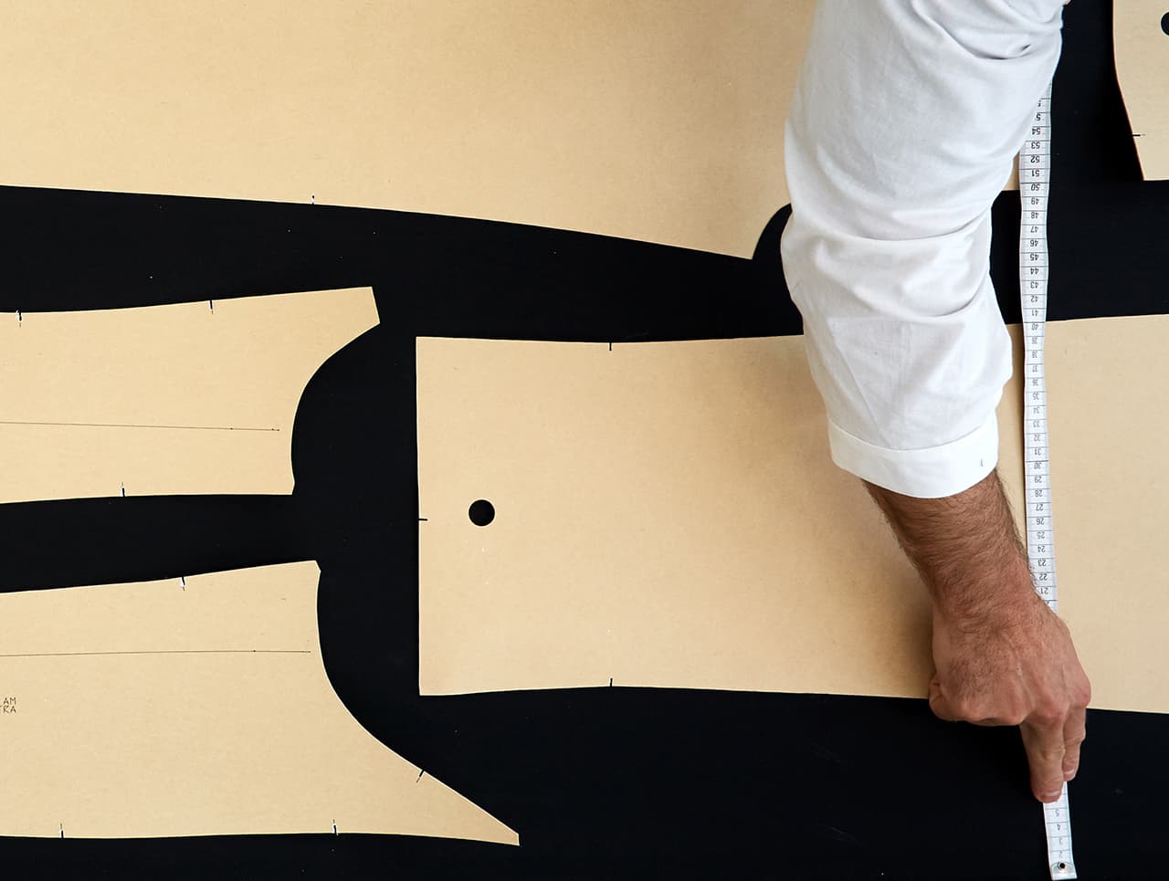 A tailor measuring fabric pattern pieces on black background with a measuring tape in Brioni.