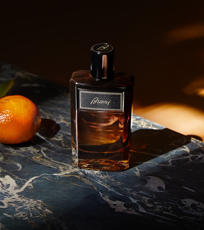 Élégant flacon marron Suave posé sur une surface en marbre sombre, avec un fruit orange à côté, sous un éclairage chaud.