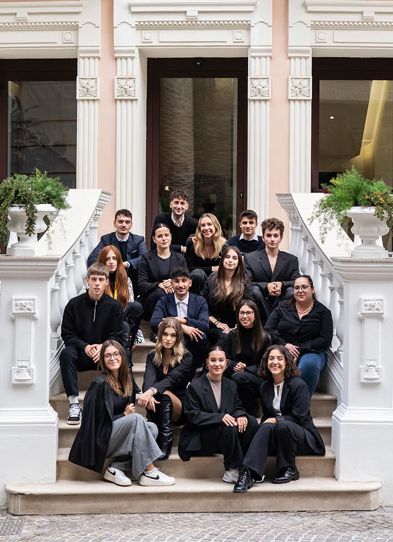 Un gruppo di studenti in abiti formali posa sulla scalinata della Scuola di Alta Sartoria.