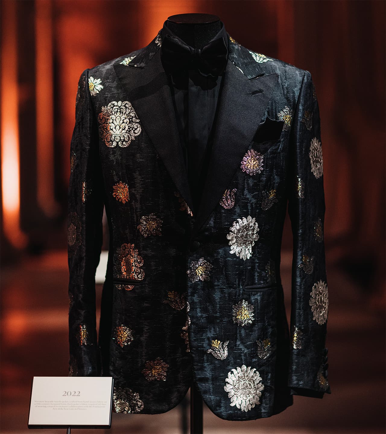 Brioni elegant black tuxedo jacket with floral metallic embroidery displayed on mannequin against warm background