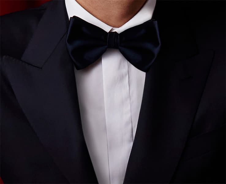 Close-up of formal attire featuring a Brioni navy blue bow tie with a Brioni black tuxedo jacket and crisp white dress shirt.