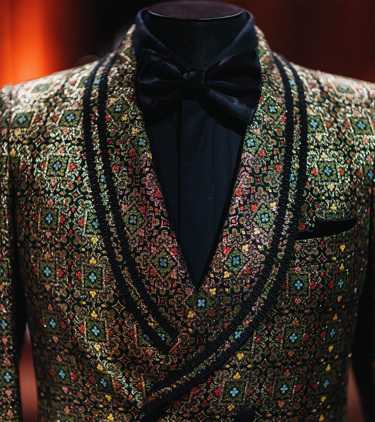 Brioni elegant formal attire featuring a colorful patterned jacket with intricate embroidery paired with a black bow tie.