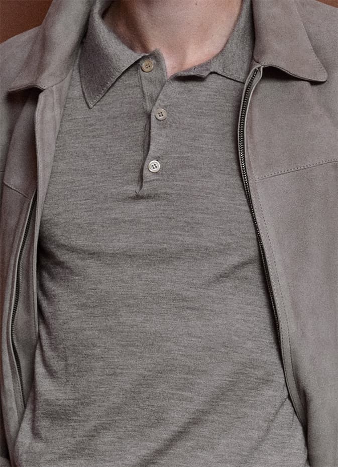 Person wearing a Brioni grey polo shirt under a light beige jacket, showing minimalist casual style.