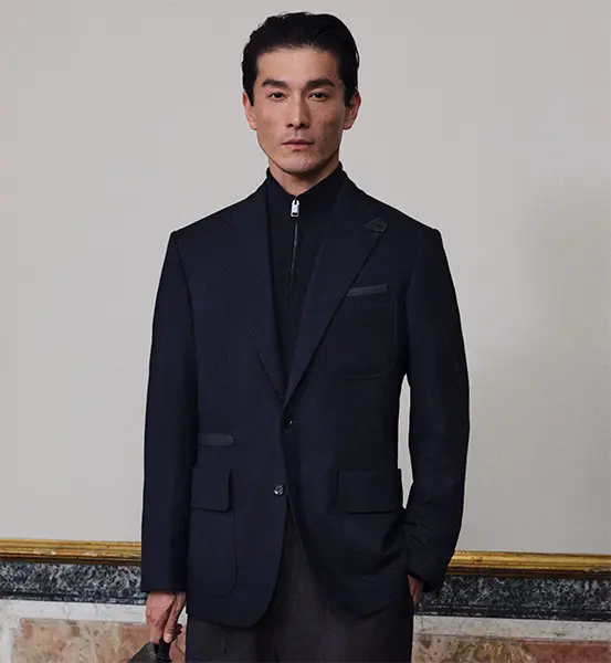 Person in elegant Brioni navy blazer with zip-up collar against neutral background, formal portrait style.